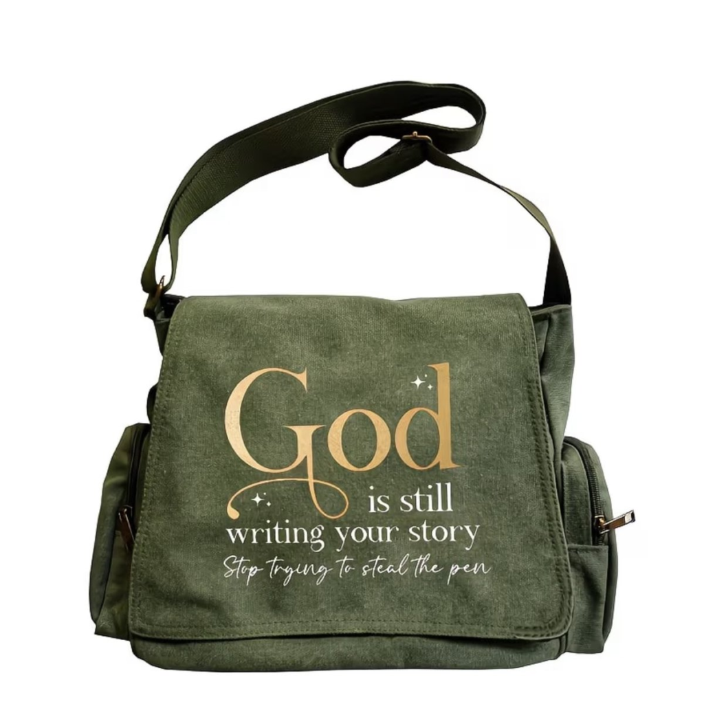 Olive green canvas messenger bag printed with God Is Still Writing Your Story in gold and white